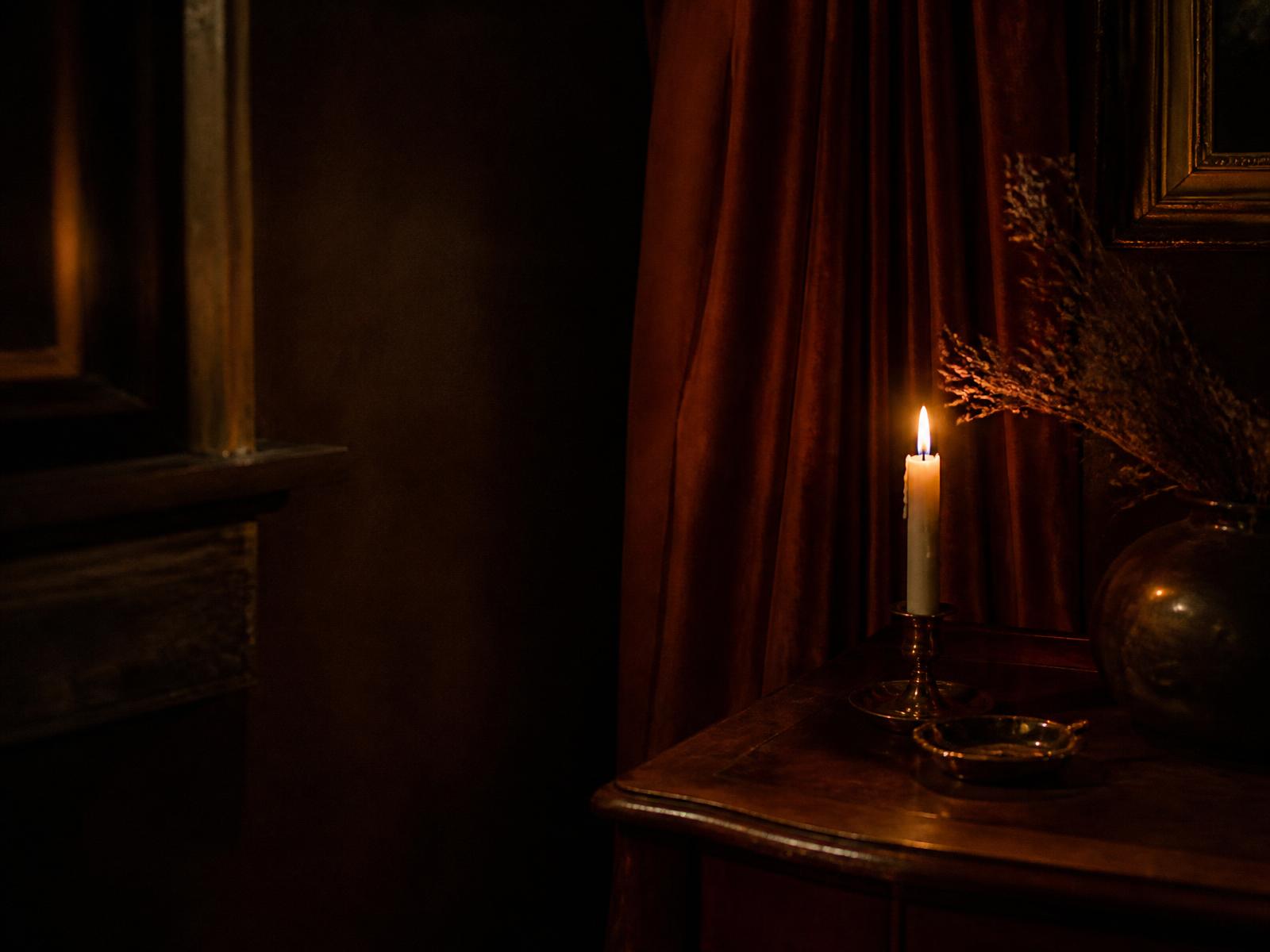 A single candle burning beside a rust-red velvet drape